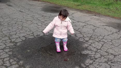 a little girl is so excited to be outside and jumping in tiny puddles in pink rubber boots