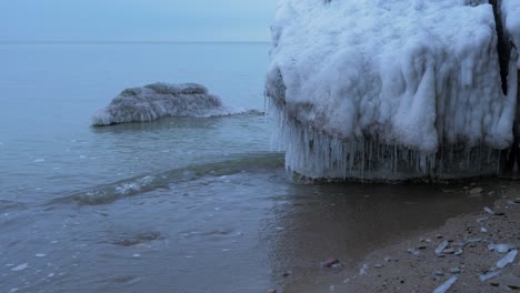 Pequeñas-Olas-Rompiendo-Contra-Las-Ruinas-De-La-Fortificación-De-Los-Fuertes-Del-Norte-De-Karosta-En-La-Orilla-Del-Mar-Báltico-En-Un-Día-Nublado-De-Invierno,-Cubierto-De-Hielo,-Nieve-Y-Carámbanos,-Plano-Medio