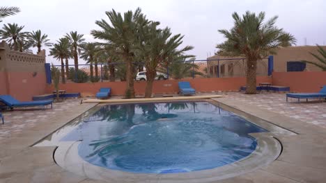 A-young-man-walking-inside-a-swimming-pool-in-the-middle-of-the-desert,-Morocco