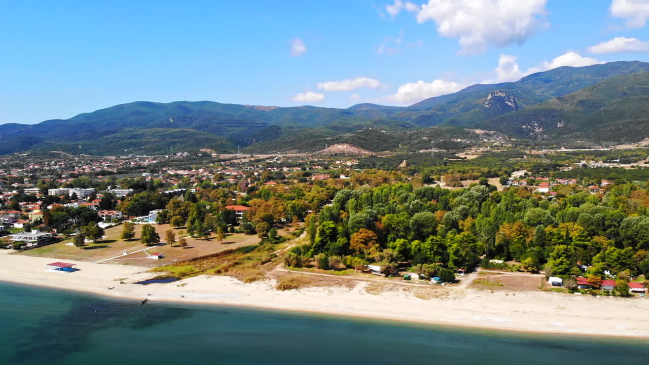 Panorama of the Asprovalta with multiple buildings and greenery, green hills on the background. Aegean sea coast. Sunny day. Greece
