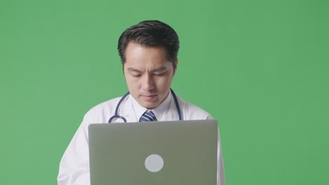병원 에서 녹색 스크린 배경 에 걸어 다니는 동안 노트북 을 사용 하는 스테토스코프 를 가진 아시아 남자 의사 의 근접 사진