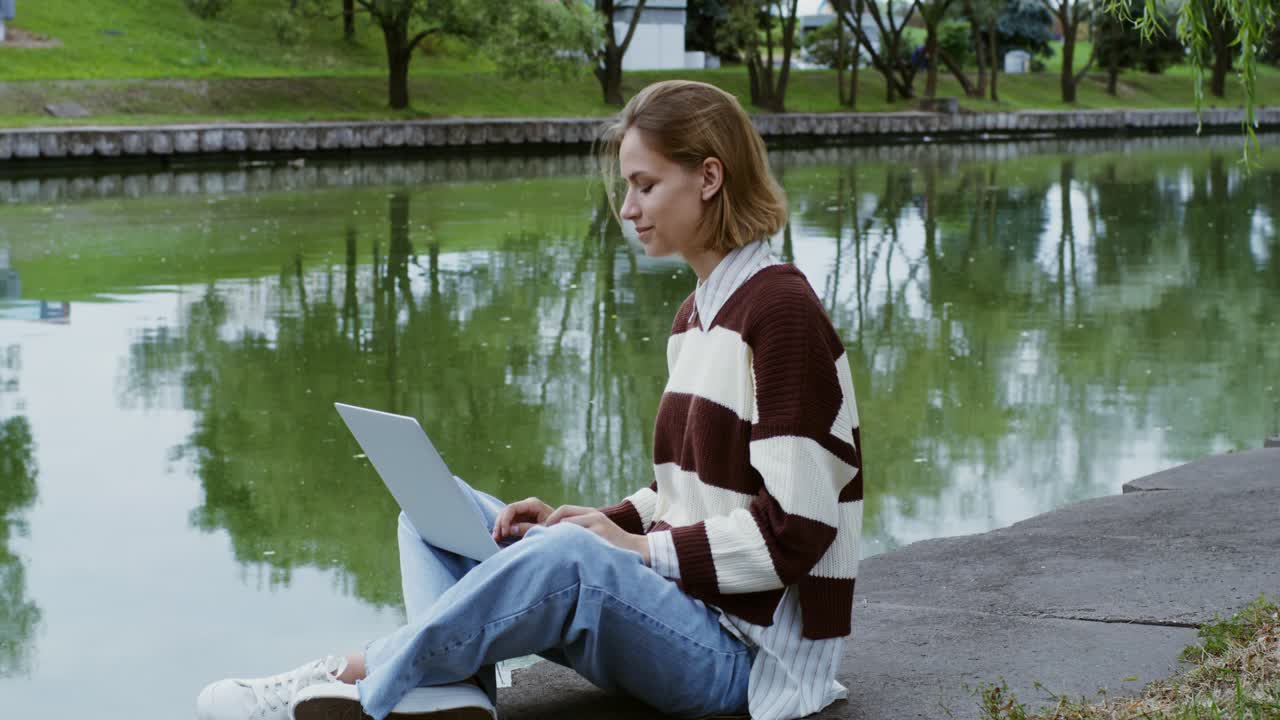 mujer trabajando en una computadora portátil en un parque junto al río