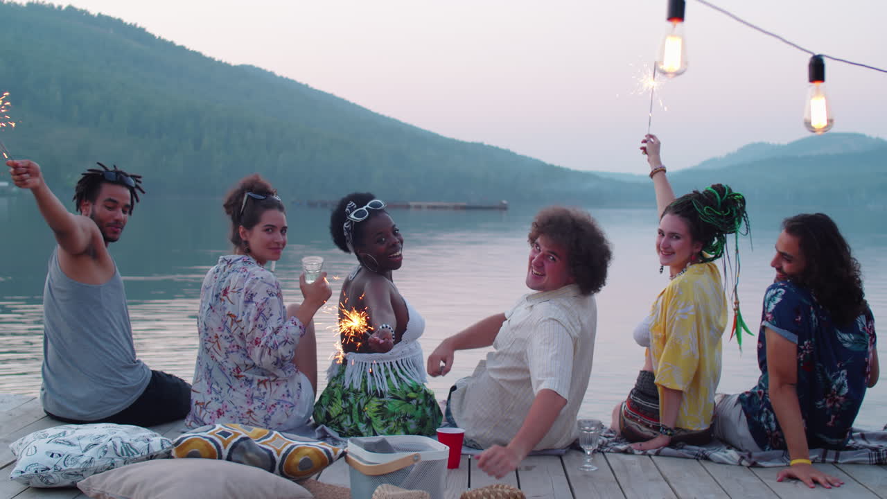 Friends Holding Sparklers and Smiling at Camera on Lake Pier