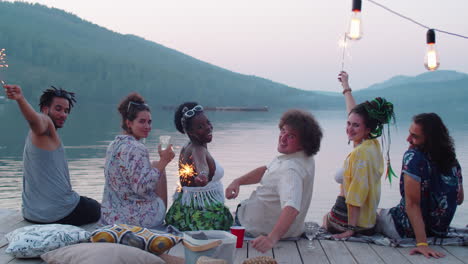 friends holding sparklers and smiling at camera on lake pier