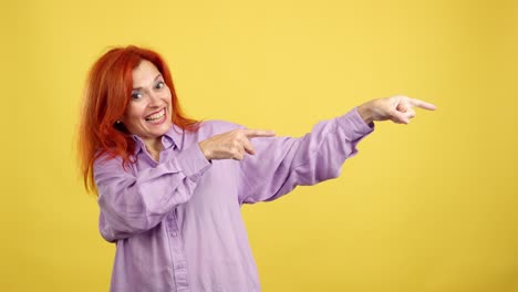 red-haired woman in purple shirt pointing to the side on a yellow background