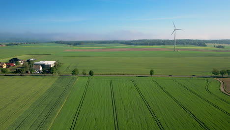 Vista-Panorámica-De-Una-Carretera-Rural-En-Un-Vasto-Campo-Verde-Con-Turbinas-Eólicas-Durante-El-Día