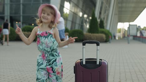 Child-girl-tourist-with-suitcase-luggage-bag-near-airport.-Kid-dances,-rejoices,-celebrates