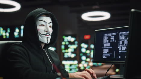 masked hacker typing keyboard breaking cybersecurity at dark datacenter closeup