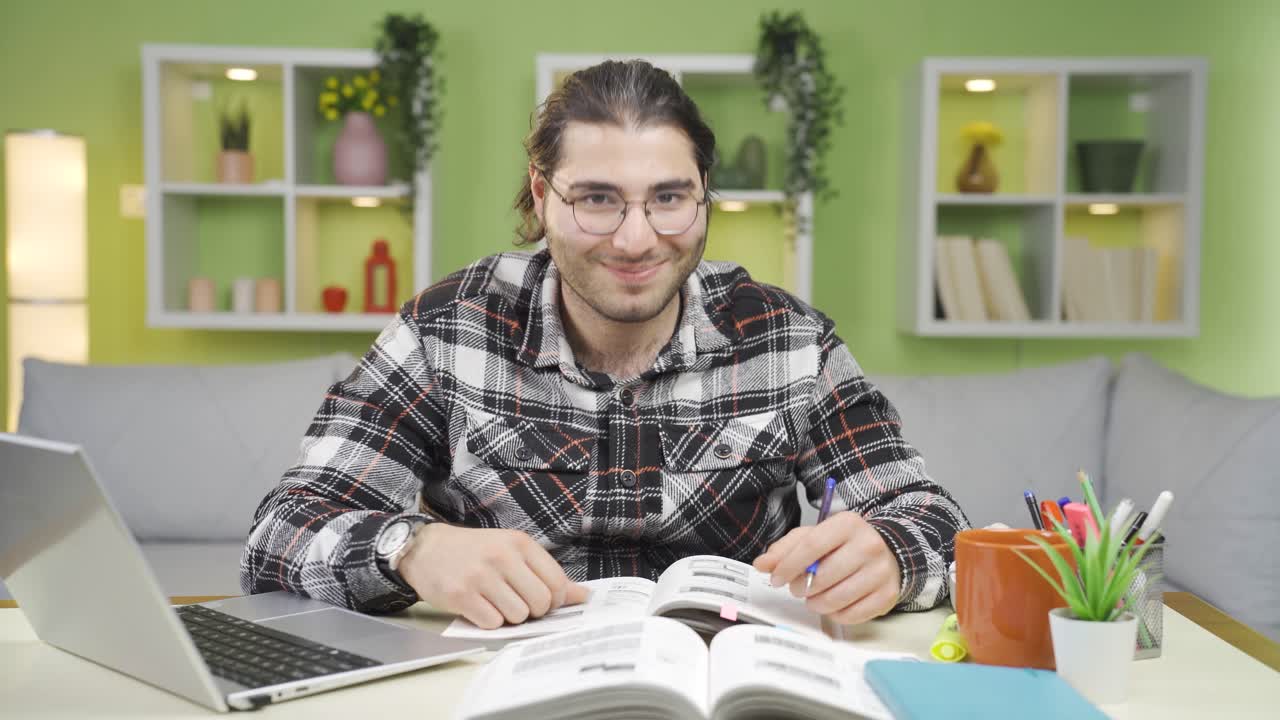 estudiante masculino feliz estudiando en el escritorio y mirando a la cámara sonriendo.