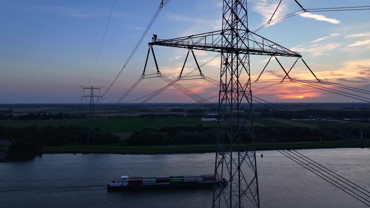 Man working high above a river on an electrical transmission tower during sunset