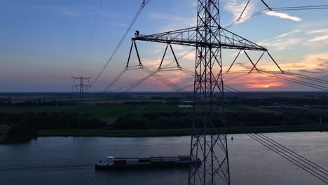 man working high above a river on an electrical transmission tower during sunset