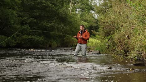 hand-held shot of a flyfisherman wading and casting into the river