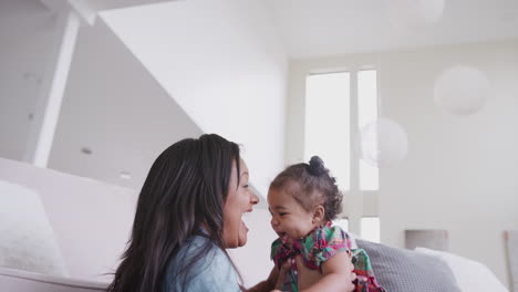 mother playing with baby daughter lifting her in the air at home
