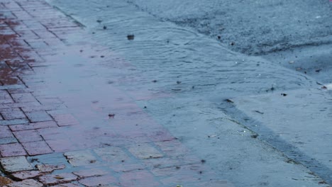 rainy weather as rain drops fall into pool between sidewalk and road, static shot