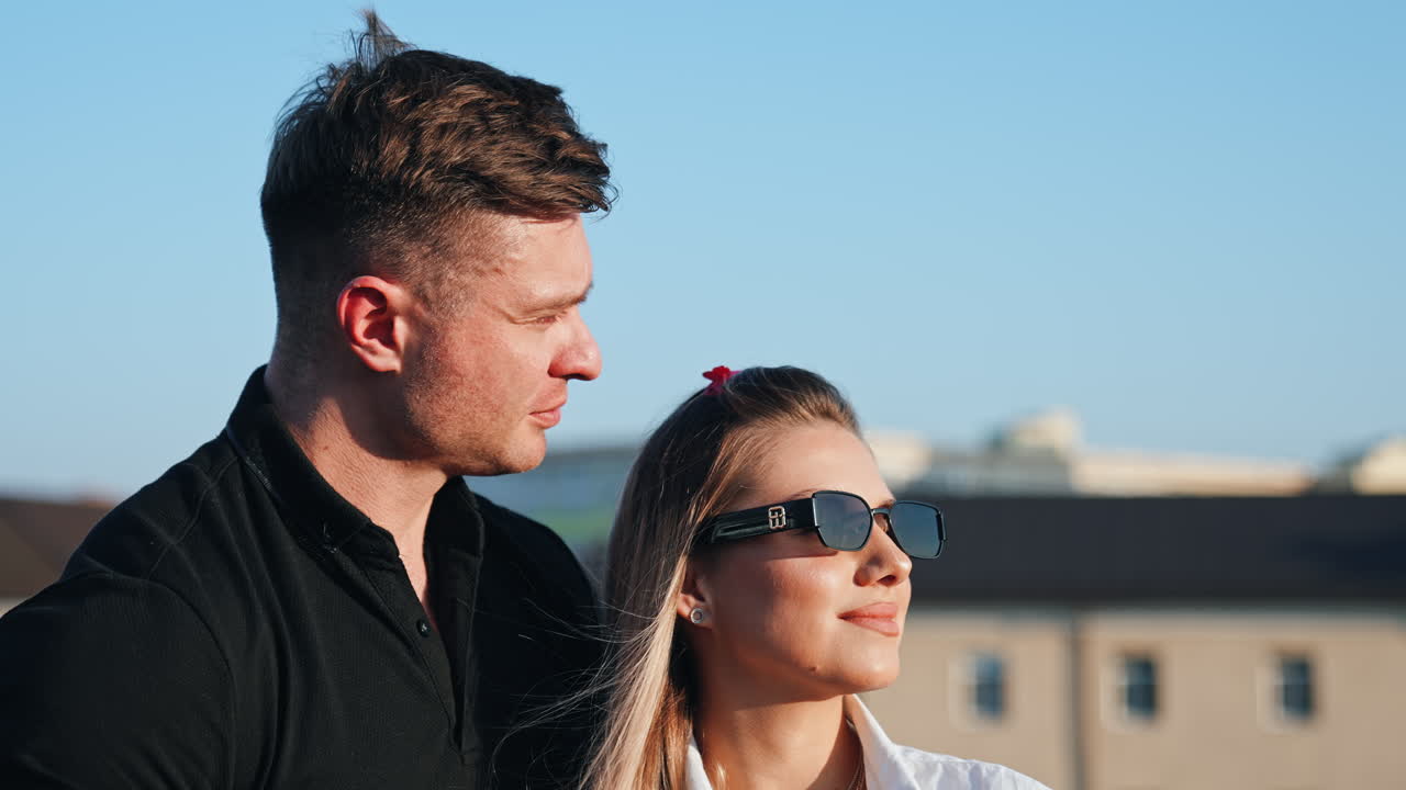 Beautiful Caucasian couple stand facing the sun. Muscular man kisses his woman wearing sunglasses.