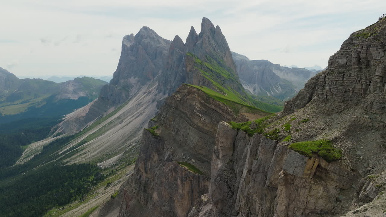 Seceda cliffs rise sharply from green slopes in dramatic golden light aerial establishing