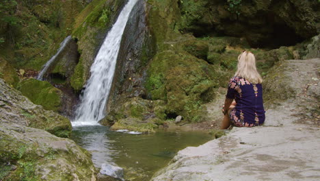 hermosa chica con cabello rubio está soñando despierto frente a la cascada