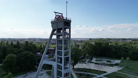 Historical-mine-shaft-during-a-beautiful-summer-day-surrounded-by-lush-greenery,-grass,-and-trees-under-a-blue-sky