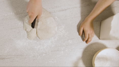 top down shot of young male chef forming sourdough dough on a kitchen side and placing it into a baking basket ready to be put into the oven