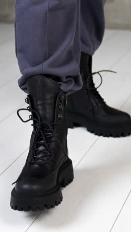 black massive army boots with laces on model's legs. woman walks in stylish footwear on the white floor in studio. top view close up. vertical video