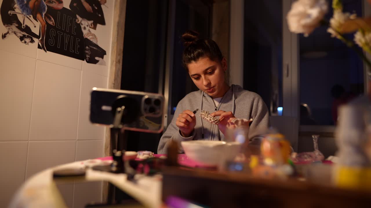 Giovane donna concentrata su un progetto artigianale mentre registra con lo smartphone
