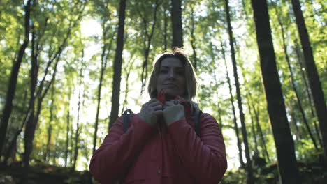 woman fastens jacket walking in autumn sunlit woods