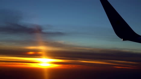 view of the sunset through the porthole of an airplane. in the right corner is visible part of the wing. beautiful orange sunset