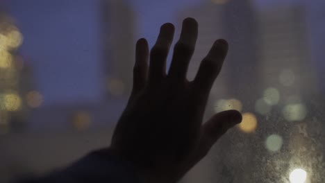 mano tocando el vidrio con las luces de la ciudad en el fondo