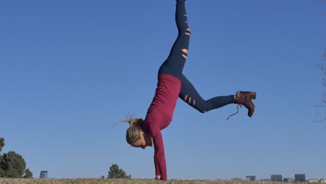 blonde woman in boots doing a handstand in the the park