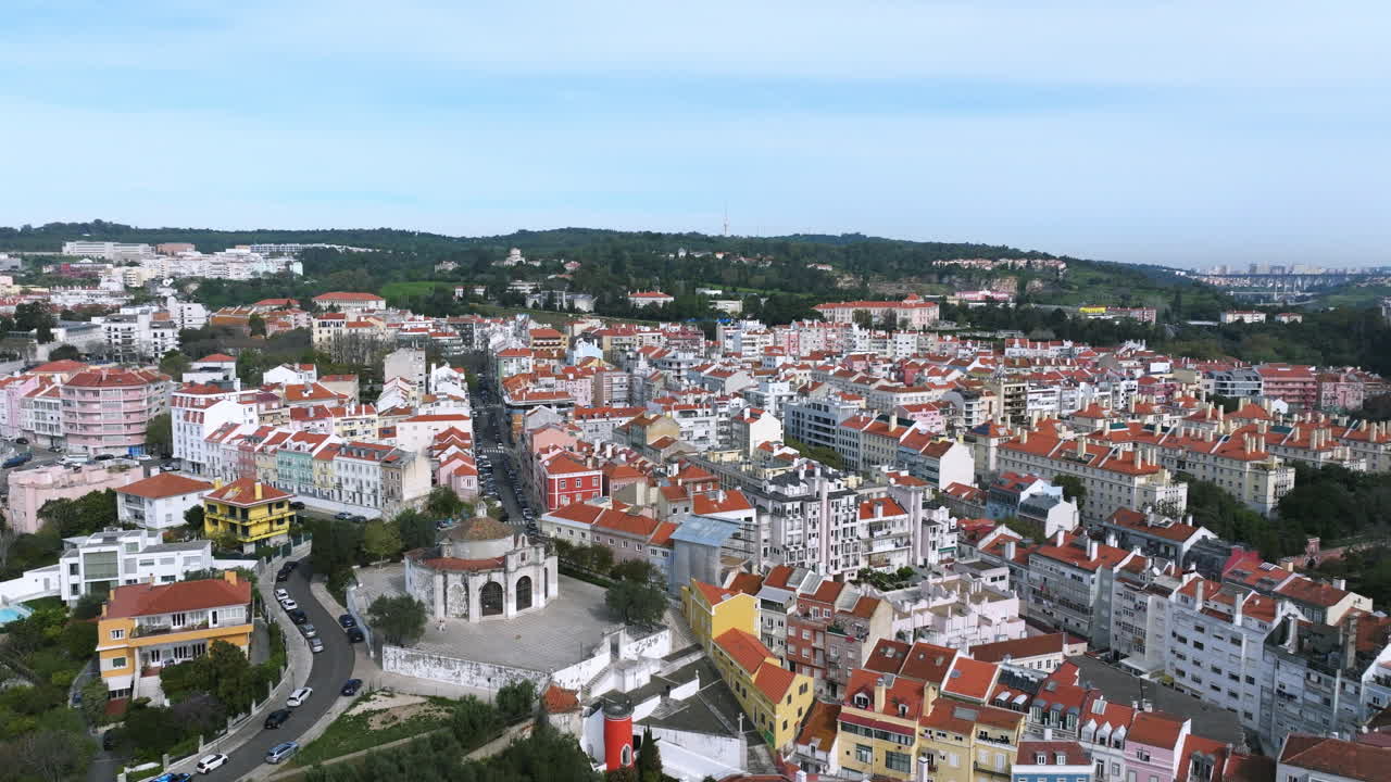 Aerial drone flight over the Lisbon cityscape on a clear morning, moving toward the Alcântara neighbourhood, Santo Amaro chapel and the green hills of Monsanto Park