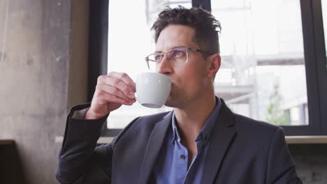 Caucasian-businessman-in-thought,-sitting-at-table-drinking-cup-of-coffee-in-cafe