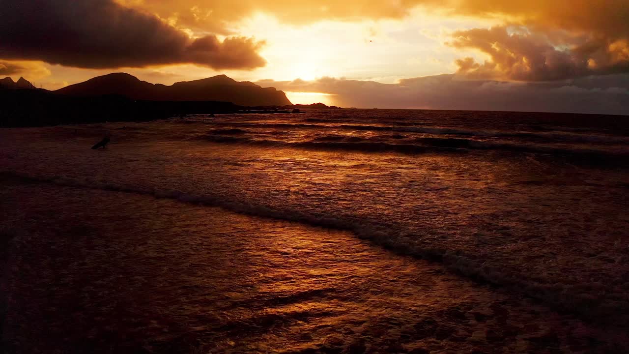 vista aérea empujando hacia las olas estrelladas de la playa de flakstad durante una impresionante puesta de sol roja dorada en las islas lofoten, noruega