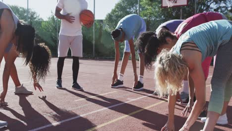 Feliz-Y-Diverso-Equipo-De-Baloncesto-Femenino-Entrenando-Con-Un-Entrenador-Masculino-En-Una-Cancha-Soleada,-En-Cámara-Lenta