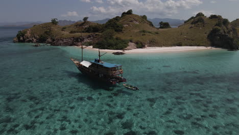 Traditional Wooden Boat Floating On Shallow Blue Sea With Coral Reef Under. Labuan Bajo In Nusa Tenggara, Indonesia. aerial orbit