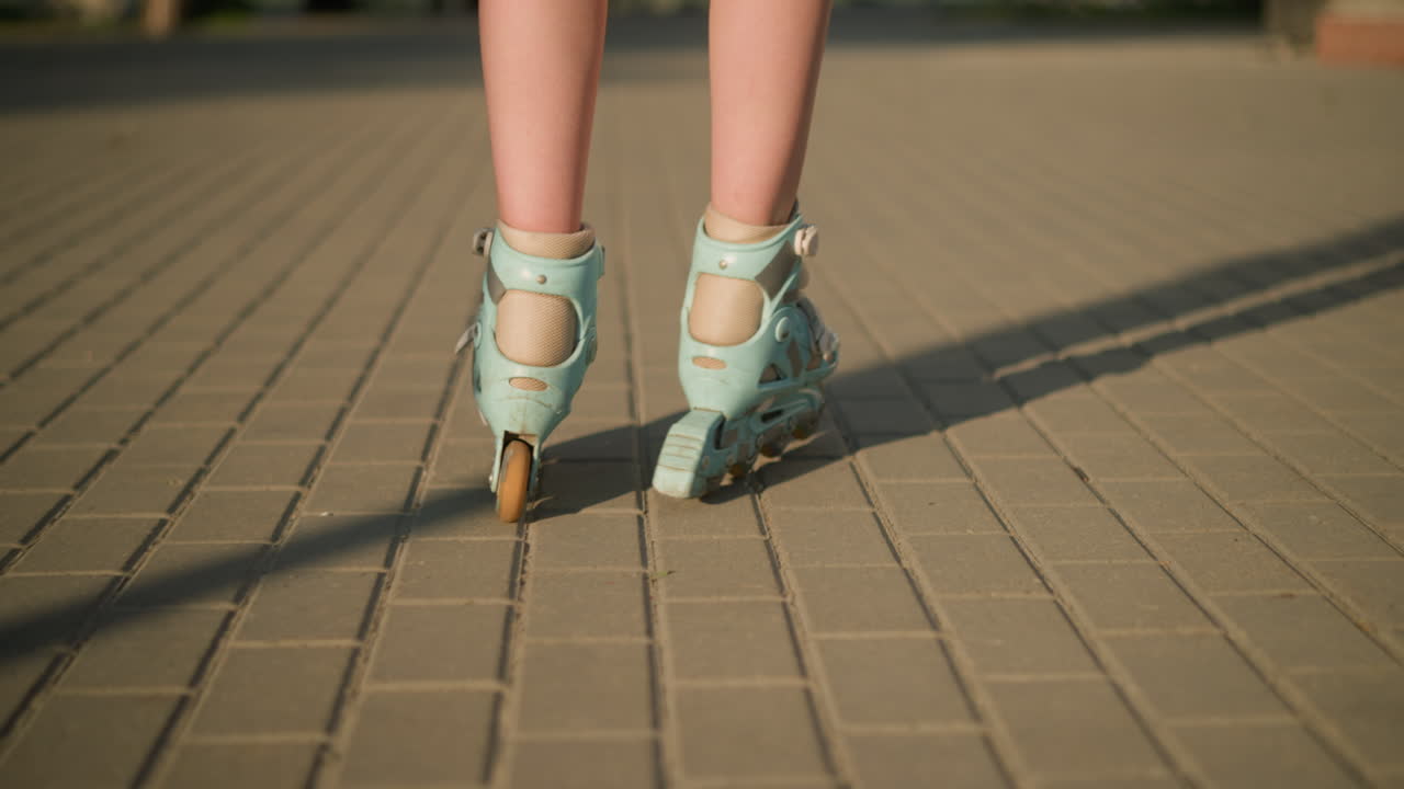 Back leg view of person skating along interlocked path on rollerblades, shadows extending on ground, with soft focus on blurred background and warm sunlight