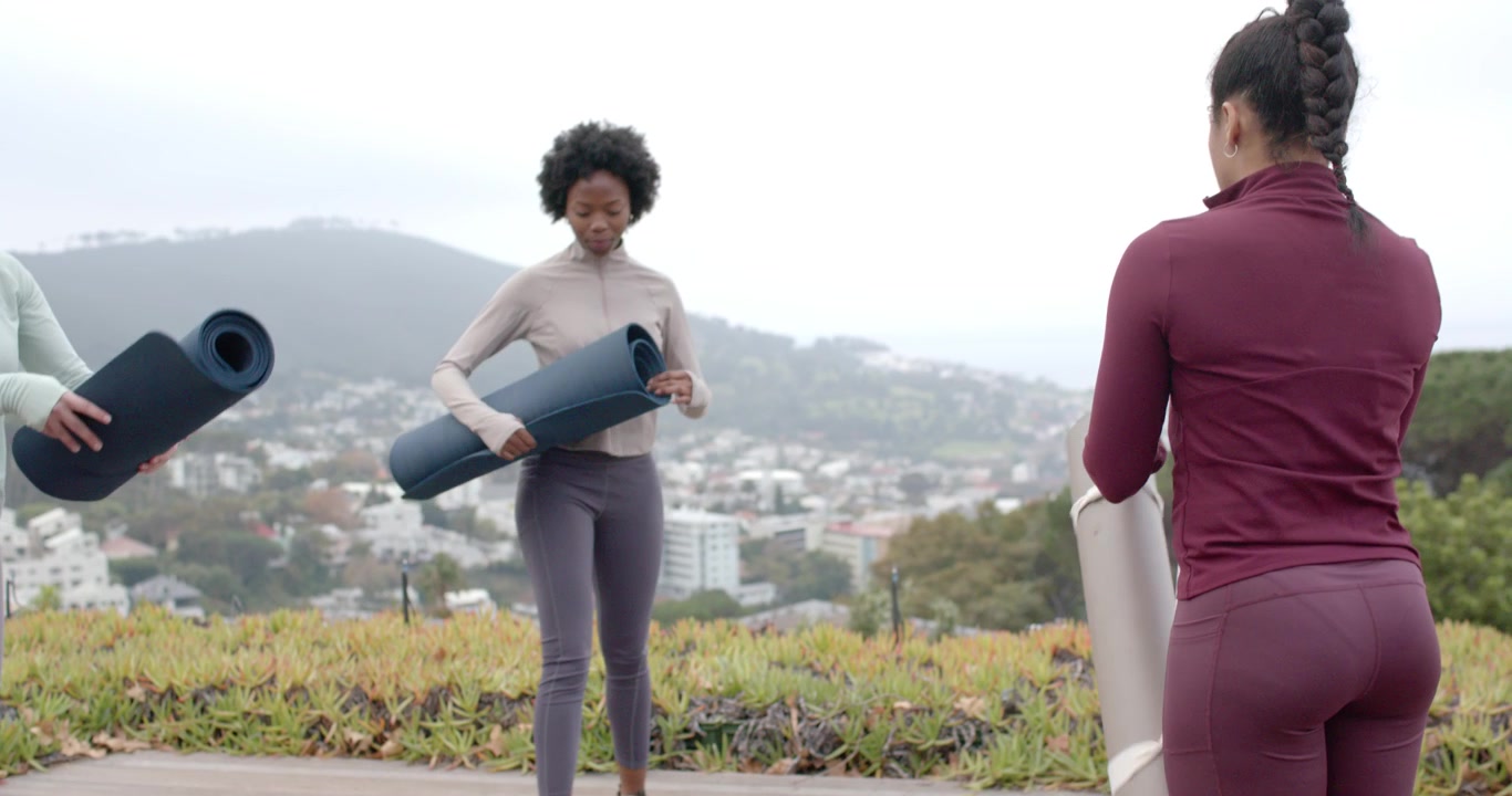 Diverse amiche arrivano su un ponte di legno, tenendo tappetini, posando una bottiglia, prendendo il telefono e preparandosi per lo yoga