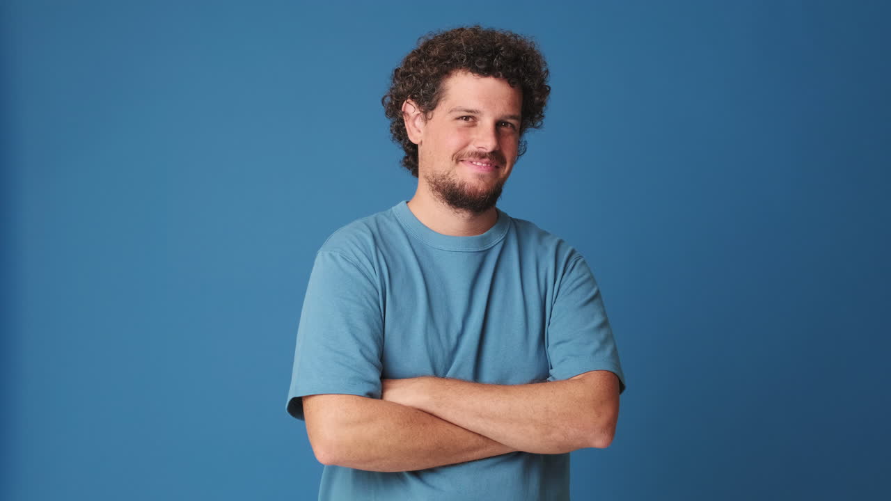 Confident Man with Curly Hair Smiles and Crosses Arms