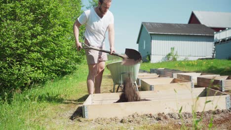 male gardener putting soil on wooden planter - wide