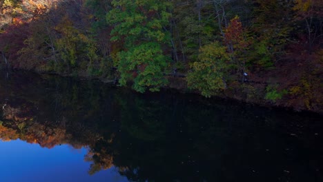 An-aerial-view-of-a-reflective-lake-in-the-morning-with-colorful-autumn-trees-on-the-bank