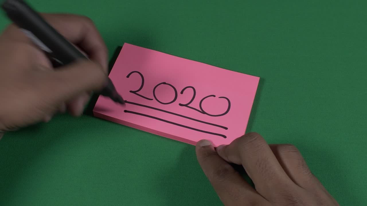 Male Left Hand Writing 2020 On Pink Post It Note And Underlining It