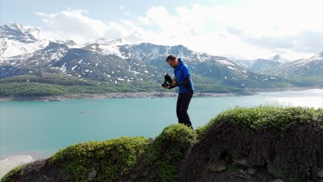 Zoom-in-on-drone-pilot-standing-on-grassy-ridge-overlooking-Mont-Cenis-Lake,-France