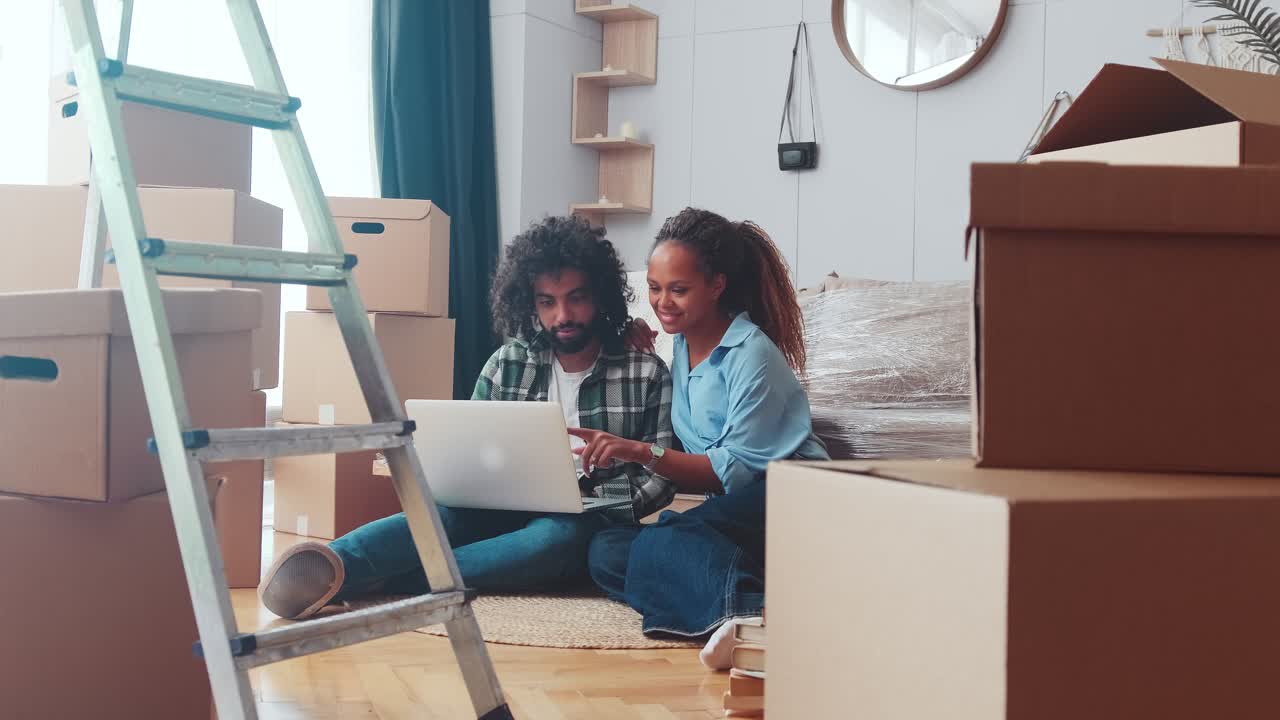 Young multiracial couple woman and man using laptop sits in home among boxes