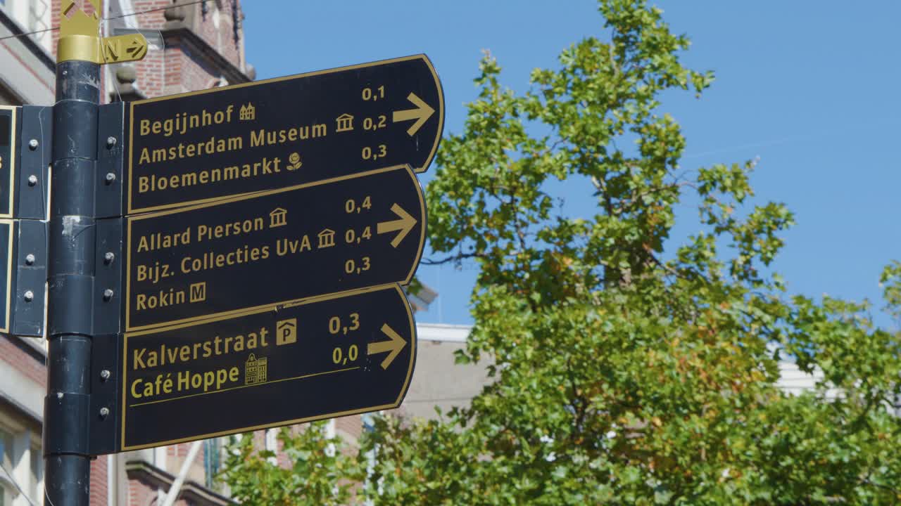 Directional street signs in Amsterdam, clear daylight, static camera, leafy urban background, blue sky