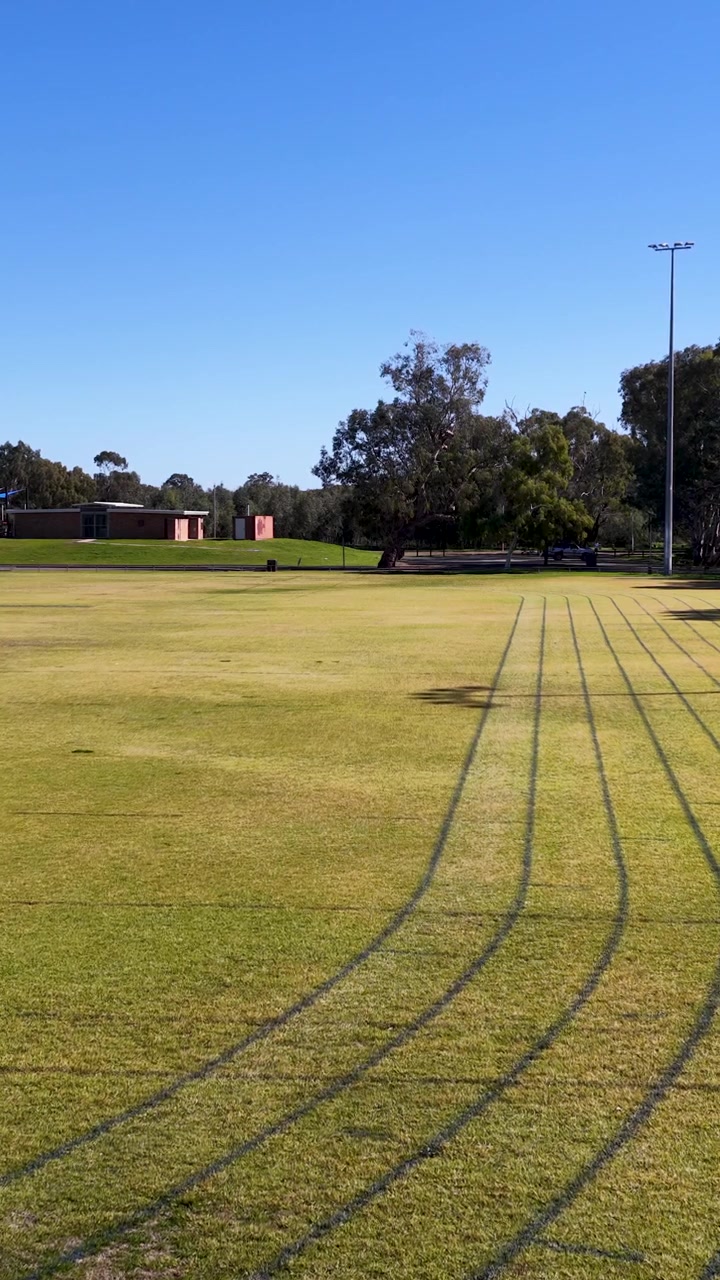 Plano geral de uma pista de atletismo oval de grama com raias pintadas sob luz solar intensa em Gunnedah