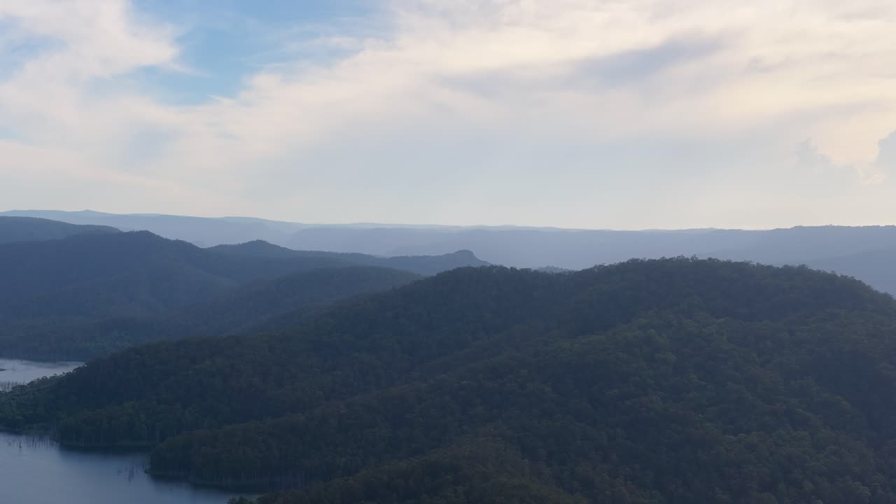 Drone pans across lush hinterland mountains, lake reservoir, and bushland under soft daylight skies