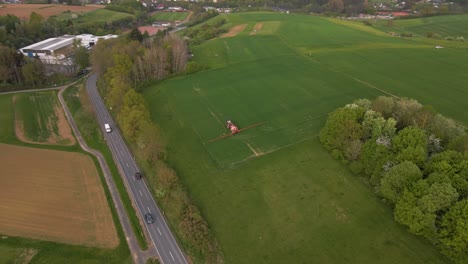 Vista-Aérea-De-Un-Granjero-Conduciendo-Su-Tractor-Sobre-Un-Enorme-Prado-Verde-Para-Rociarlo-Con-Agua-O-Pesticidas