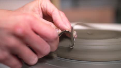 close-up shot of hands doing pottery in slow motion, trimming a plate with a tool, clay plate turning on the wheel