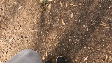 looking down at a man's feet in black runners walking along a dirt trail