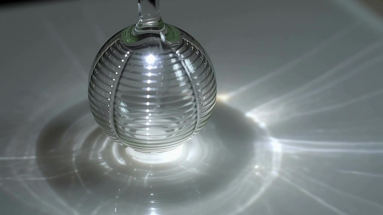 Rotating ribbed glass sphere on short stem above tabletop, focused light creating shifting caustics