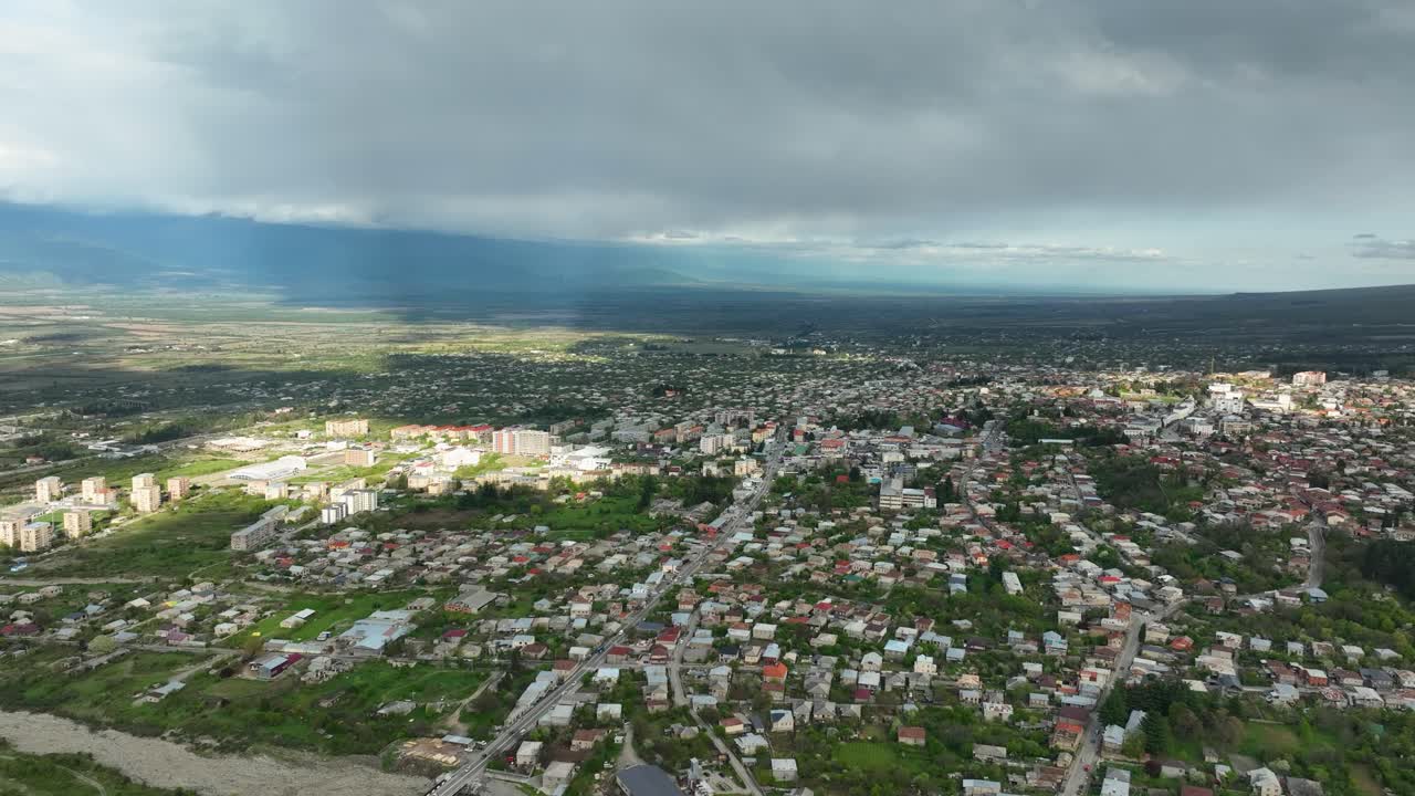 Широкая панорама с воздуха грузинского города, раскинувшегося в долине с горами, с переменчивыми погодными условиями